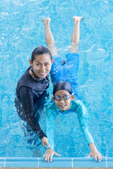 Cute asian little girl learning to swim with coach at the leisure center