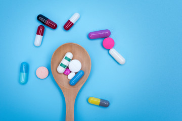 Capsules tablets on wooden spoon blue background.