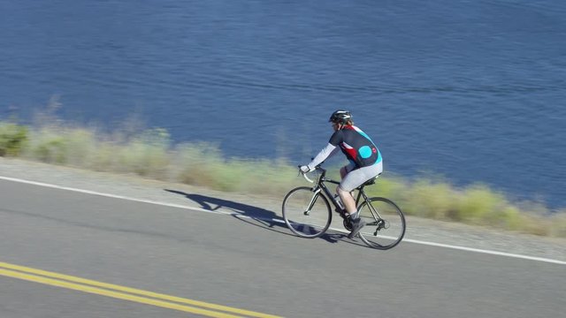 Man riding bicycle on country road overlooking lake