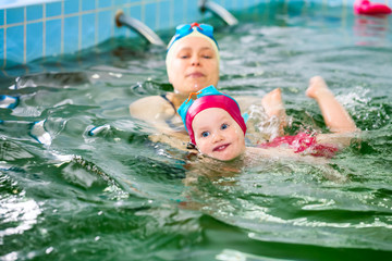 Little girl learning to swim with mother's help in a seawater swimming pool