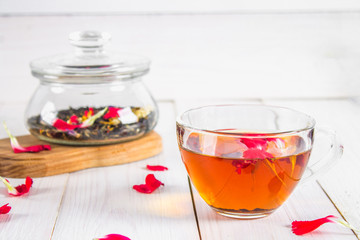A cup of tea, in the background of a bank with a black herbal floral tea on a white wooden table.