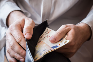 Man's hand holding a black wallet with euro money.