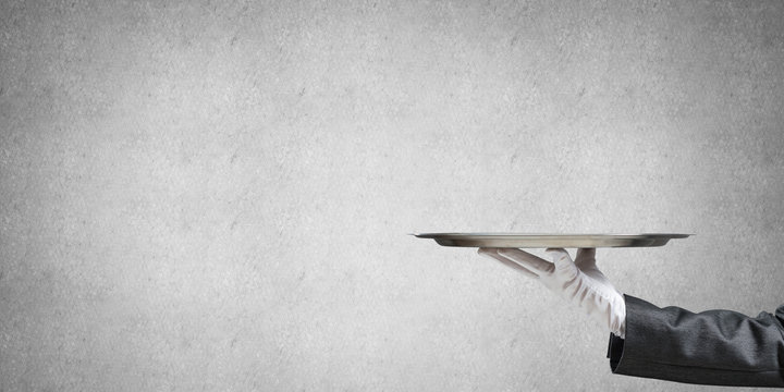 Hand of butler holding empty metal tray against concrete background