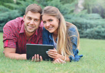 Happy couple lying in the park using tablet pc together
