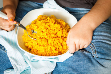Child (girl) eats a boiled bulgur from a wooden bowl. Love for a healthy vegan food concept
