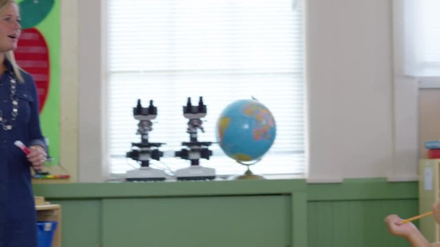 Teacher gives lesson in school classroom and students raise hands