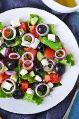 Classic Greek salad with sauce on a blue old background.