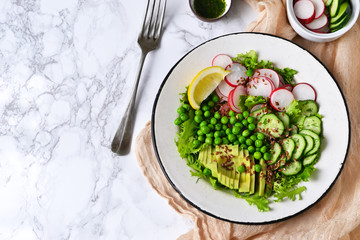 Mix salad with cucumber, avocado, green peas and flax seeds on a marble background