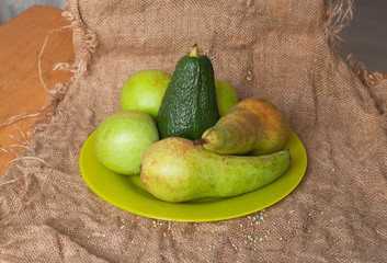 A plate with an avocado, green apples, pears on the sackcloth texture background