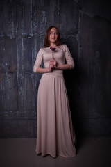 Beautiful elegant young woman with flower in hands standing in front of dark vintage wall.