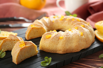 Board with sliced citrus cake on brown wooden background