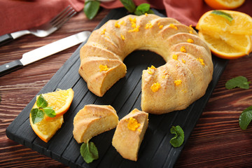 Board with sliced citrus cake on brown wooden background