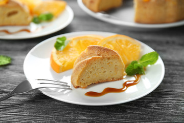 Plate with piece of citrus cake and fresh orange slices on wooden table