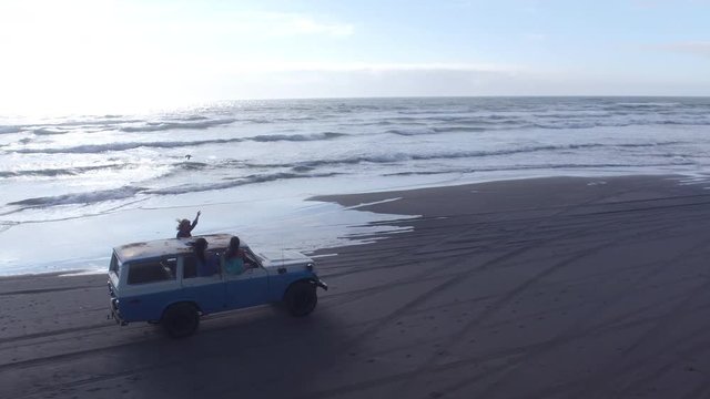 Aerial View Of Group Of Friends Driving On Beach In Vintage Vehicle