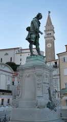 Obraz premium A main square in the town of Piran. A statue of a musician in the front and an old church in the background.