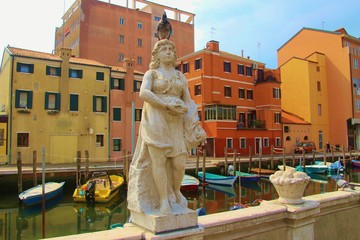Statue of a roman goddess with vines, a pigeon sitting on her head. On a canal in Chioggia, North Italy, Europe.
