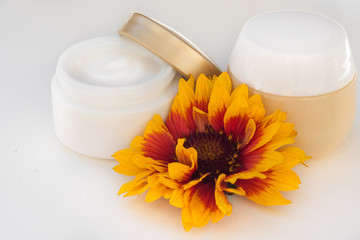 Cosmetic cream container and yellow flowers on white background.