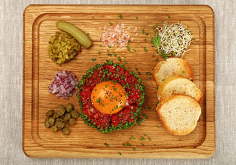 Raw meat tartare steak with egg yolk on wood board