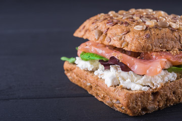 Rye sandwich with fish salmon with tomatoes and cream cheese. Wooden black background. close-up