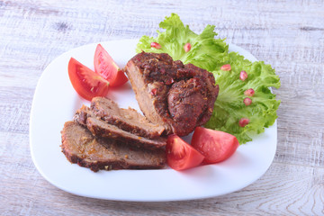 Steak of grilled meat with tomato, lettuce and beans pomegranate on white plate.