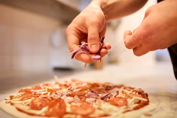 Fotobehang kook het toevoegen van ui aan salami pizza bij pizzeria © Syda Productions