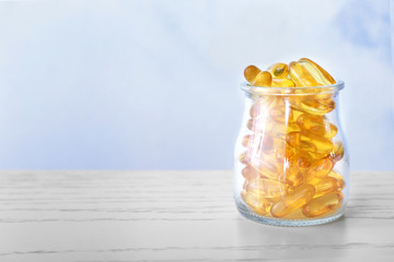 Glass jar with fish oil capsules on table