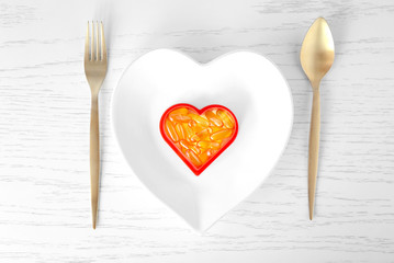 Heart-shape plate with fish oil capsules on wooden background