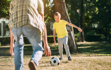 Eight year old boy playing football in a park with dad