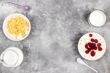 Cottage cheese in bowl with frozen raspberry and cup of cornflakes, milk in glass on a light background. Top view, copy space. Food background