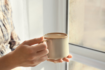 Fototapeta na wymiar Woman with cup of hot tea near window, closeup
