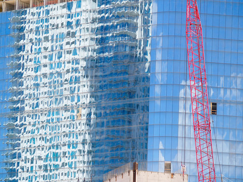 Distrorted and blurry images adjacent buildings and red construction crane working and reflected in large glass windows of building