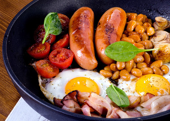 Full English breakfast with fried eggs, sausages, bacon, beans, toasts and mushrooms.