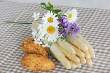 Spargel mit Frühkartoffel hübsch dekoriert mit Schnittlauchblüten und Margaritten auf kariertem Tuch