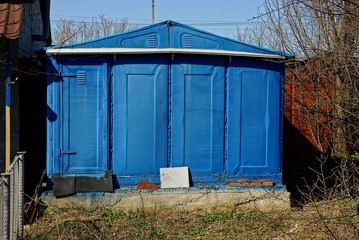 Синий металлический гараж во дворе в солнечный день
