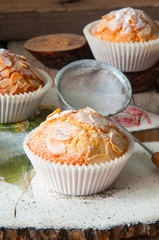 Close up of freshly baked almond and apricot muffins sprinkled with sugar powder and almond petals in a rustic setting on the decorated wooden board.