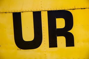 Letters on a yellow painted metal texture with rivets