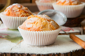 Close up of freshly baked almond and apricot muffins sprinkled with sugar powder and almond petals in a rustic setting on the decorated wooden board.