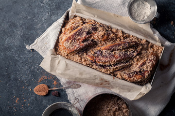 Chocolate babka on blue rustic background. Homemade cocoa bun on parchment paper with baking utensils. Traditional french cuisine