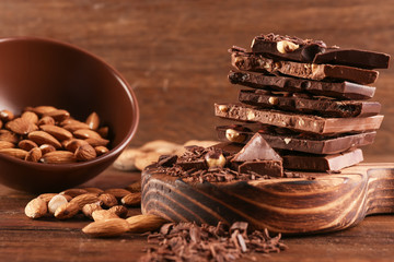 Cutting board with pile of chocolate, bowl and nuts on wooden background