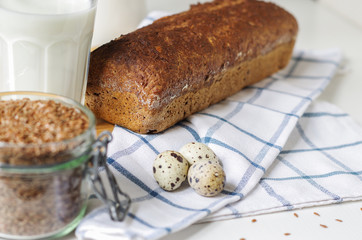 Homemade gluten free bread with linseed flour and psyllium husk. Jug and glass of milk, linen seed in glass jar
