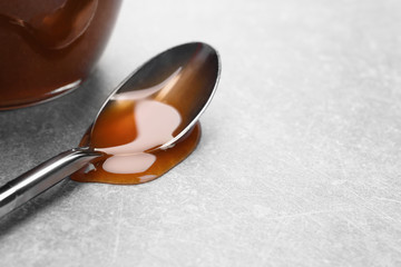 Spoon with tasty caramel sauce on light background, closeup