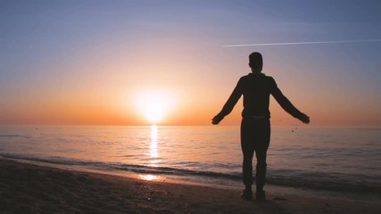 Young athletic man doing gymnastics on the sea early in the morning