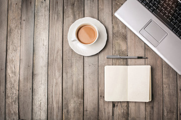 Wooden table with a laptop, a cup of coffee, a book and a pen on it