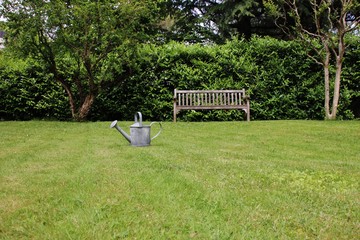 Steel watering can in an italian garden with wooden bench