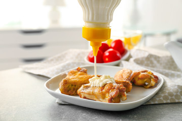 Pouring mayonnaise sauce into plate with tasty chicken wings, closeup