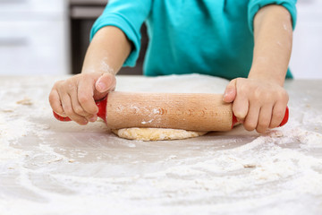 Little girl rolling out dough on kitchen table, closeup