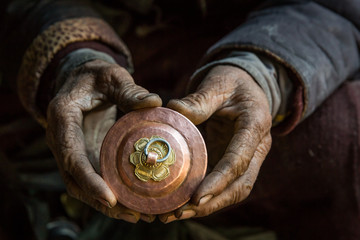 An old craftsman is holding in his hand a cup, traditional Tibetan copper handicraft product in his...