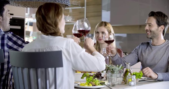 Italian people making toast together with red wine. Four happy real candid friends enjoy having lunch or dinner together at home or restaurant. 4k video