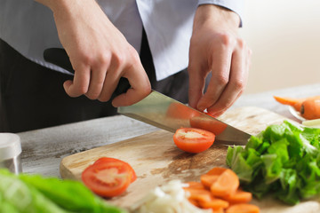cooking and home concept - close up of male hand cutting tomato on cutting board with sharp knife