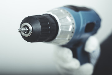 Electric screwdriver in hand at white desk background